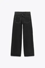 Pantalón de jean negro de tiro alto con pierna ancha y detalle de tachas plateadas en los bolsillos y laterales.