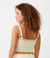 Top cropped de punto color crema con detalles de rayas contrastantes en color mostaza. Presenta escote en V, tirantes finos regulables y un diseño texturizado con calados. El bajo es festoneado y ondulado.
