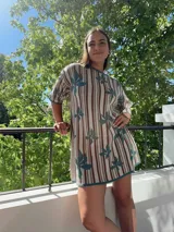 Vestido tejido de algodón con diseño de rayas verticales en tonos beige, marrón y verde azulado, con motivos de hojas grandes en verde azulado. Tiene cuello redondo y manga corta, con un calce holgado.