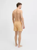 Short de baño naranja con rayas verticales blancas y estampado de tiburones azules. Cuenta con cintura elástica ajustable con cordón blanco.