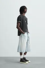 Camiseta negra de corte holgado, cuello redondo y manga corta. Estampado frontal con texto en blanco y parche rectangular en la espalda. Efecto lavado.