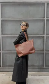 Cartera tipo tote de cuero graneado color negro, con textura uniforme y suave al tacto. Tiene manijas de 55 cm, bolsillo frontal con broche imantado, bolsillo trasero con cierre metálico, cierre principal metálico, forro interior y tres bolsillos internos (uno con cierre, uno plaqué y uno tipo sobre con solapa y botón).