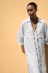 Vestido camisero largo color verde claro, confeccionado en lino. Tiene cuello solapa, escote en V, manga tres cuartos con trabilla y botón, bolsillos delanteros de plastrón, aberturas laterales en el ruedo y cierre frontal con botones.