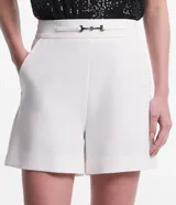 Short de vestir blanco de corte sastrero, con cintura alta, bolsillos laterales y detalle de hebilla metálica plateada en la cintura.