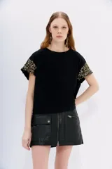 Remera negra de jersey 100% algodón con cuello redondo y manga corta caída. Las mangas están completamente bordadas con lentejuelas negras.