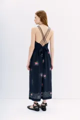 Vestido midi negro con estampado floral y puntos blancos. Presenta escote pronunciado en la espalda con múltiples tiras finas cruzadas que se atan con un lazo en la cintura.