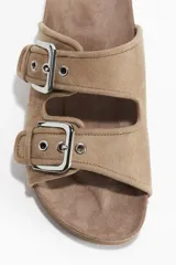 Sandalias planas color beige de gamuza sintética, con dos tiras anchas ajustables mediante hebillas metálicas plateadas.