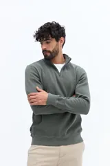 Buzo de algodón color verde musgo, con cuello alto y cierre frontal parcial. Presenta puños y cintura acanalados, y un pequeño logo bordado en el pecho.