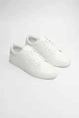 Zapatillas acordonadas blancas de cuero sintético, con suela plana de goma y cordones blancos.