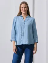 Camisa celeste de tencel con cuello con solapa, escote en V, abertura central con botones y mangas 3/4 regulables con presilla y botón.