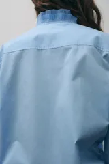 Camisa blanca de algodón con cuello con volantes y mangas largas con puños fruncidos.