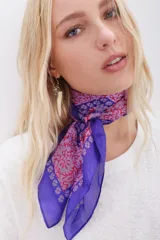 Pañuelo cuadrado de seda color violeta con estampado floral en tonos rosados y detalles geométricos en azul.