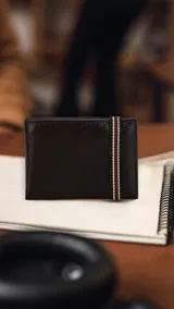 Billetera de cuero lisa color marrón oscuro con un galón elastizado tricolor (verde, blanco y rojo) en el exterior. El interior cuenta con compartimentos para billetes, un visor y tarjeteros.