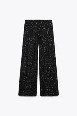 Pantalón negro de tiro alto con lentejuelas, corte palazzo y cierre frontal con cremallera, botón interior y gancho metálico.