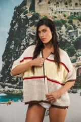 Remera de tejido calado color crudo con rayas horizontales rojas y terminaciones marrones, con cierre frontal y logo bordado.