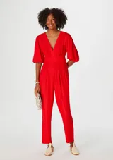 Mono rojo con escote en V, mangas cortas abullonadas, cintura ajustada y pantalón recto con pinzas.