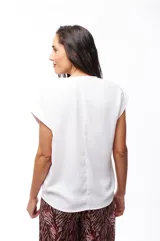 Blusa blanca de poliéster con cierre dorado en el escote y mangas cortas.