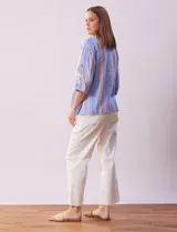 Blusa de algodón a rayas verticales en tonos celeste, rosa y blanco. Tiene cuello redondo con escote en V y abertura con botones de madera. Las mangas son 3/4 con aplique de botones.