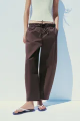 Pantalón marrón tipo barrel, de tiro medio con cintura elástica ajustable con lazada, bolsillos laterales y falsos bolsillos de vivo en la espalda.