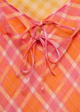Vestido corto con estampado de cuadros color naranja, rosado y amarillo, con tirantes finos y lazo decorativo en el escote.