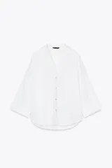 Camisa blanca de lino con cuello solapa, escote pico, manga ancha por debajo del codo con vuelta y bajo asimétrico.