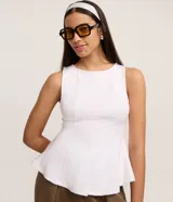 Blusa sin mangas color negro, confeccionada en tejido punto roma, con breteles anchos y corte peplum alargado que se ajusta al cuerpo en el busto y se abre en el ruedo.