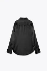 Camisa negra de satén con cuello solapa, manga larga, bolsillos con solapa en el delantero, bajo asimétrico y cierre frontal con botones.