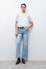 Camisa blanca de manga corta con cuello mao y detalles de bordado en el canesú superior. Presenta frunces en el pecho y la espalda, y un cierre frontal de botones.