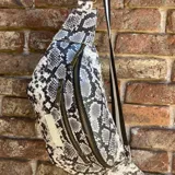 Riñonera con estampado de piel de serpiente en tonos grises y blancos, con correa regulable de rayas verticales blancas y negras.