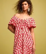 Vestido corto de viscosa y lino con estampado de olas en color blanco sobre fondo rojo. Tiene escote off-shoulder, mangas cortas holgadas, lazo en el busto con detalle de abalorios y volado en el bajo.