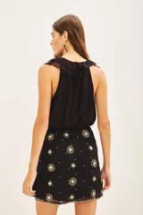 Minifalda negra con short interno, de corte cruzado con lazo lateral y bordados florales en frente y espalda.