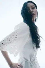 Vestido corto blanco de crepé con secciones de broderie, cuello camisero, botones ocultos, mangas cortas abullonadas, cinturón extraíble y ribete festoneado.