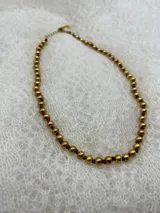 Collar corto de perlas doradas con hilo de seda azul marino y cierre de mosquetón dorado con cadena de extensión.