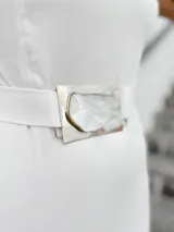 Vestido corto blanco con un hombro descubierto y una manga larga abullonada. Incluye cinturón con hebilla de alpaca y nácar.
