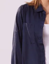 Camisa blanca de lyocell, marca Dash. Tiene cuello con solapa, abertura central con botones, mangas largas regulables con presilla y botón, y dos bolsillos delanteros aplicados.