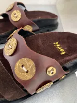 Sandalias marrones de cuero y gamuza, con apliques de monedas doradas.