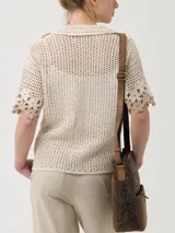 Sweater tejido a crochet color crema con flores bordadas en tonos beige y marrón. Tiene cuello camisero, mangas cortas y cierre frontal con botones.