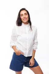 Camisa blanca de algodón con cuello alto con volados, mangas largas abullonadas y cierre frontal con botones.