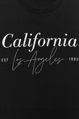 Camiseta negra de algodón con cuello redondo, manga corta y estampado frontal con la frase "California Los Angeles EST 1895" en color blanco.