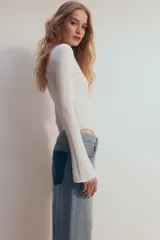 Body blanco de punto acanalado, con escote redondo, tapeta de botones y mangas largas acampanadas.