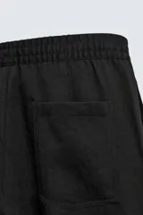 Pantalón negro de corte relajado con cintura elástica ajustable y pliegues en la parte delantera. Presenta bolsillos laterales y bolsillos traseros de parche.