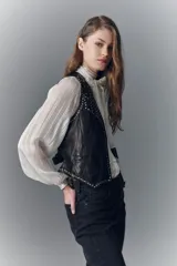 Chaleco negro de cuero ovino con tachas metálicas, botones al frente, bolsillos ojal y tira de ajuste en la espalda.