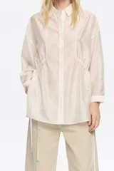 Camisa color crudo de corte ajustado en cintura, con cuello camisero, manga larga con puño y botón, cierre frontal con botonadura y túneles ajustables con tiras de tejido.