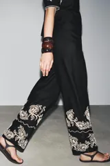 Pantalón culotte negro de lino y viscosa con bordados florales en el ruedo. Tiene tiro medio, cintura con trabillas, bolsillos laterales y cierre frontal con cremallera y botón.