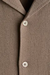 Camisa de manga corta color marrón claro, de punto texturizado de mezcla de algodón, con cuello abierto, tapeta lisa y bajo recto.
