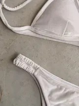Conjunto de bikini blanco con textura, compuesto por un corpiño de triángulo fijo con breteles regulables y almohadillas desmontables, y una bombacha vedetina con frunce elástico en los costados.
