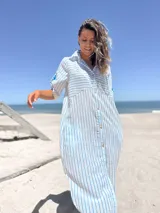 Vestido camisero largo a rayas verticales celestes y blancas, con cuello camisero, mangas cortas con botón y bolsillos laterales.