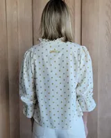 Blusa color beige con cuello con volados, mangas largas abullonadas con puños elásticos y cierre con botones en la parte delantera.