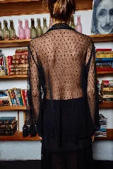 Camisa negra de tul elastizado, corte clásico y holgado, con cuello solapa, abotonada y mangas evasé muy largas para atar.