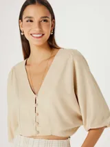 Blusa beige con escote en V, mangas 3/4 abullonadas y cierre frontal con botones.